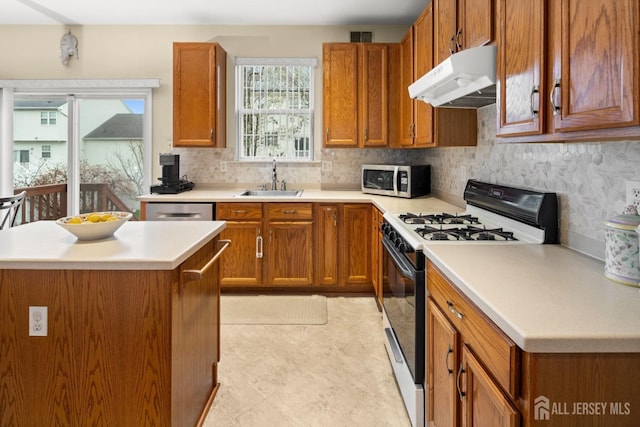 kitchen featuring under cabinet range hood, light countertops, a sink, stainless steel appliances, and brown cabinets