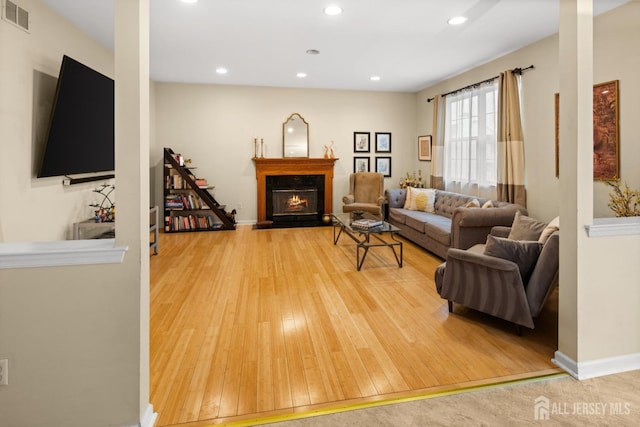 living room with visible vents, baseboards, a warm lit fireplace, recessed lighting, and wood-type flooring