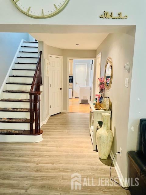 hallway featuring stairs, light wood-type flooring, and baseboards