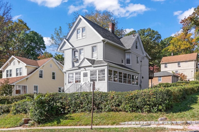 view of front of home with roof with shingles, a chimney, a sunroom, and cooling unit