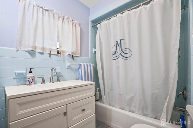 bathroom featuring toilet, shower / bath combo with shower curtain, tile walls, and vanity