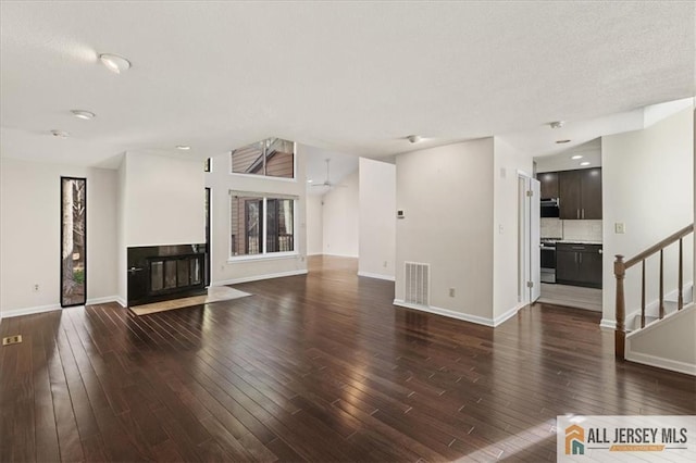 unfurnished living room featuring visible vents, a fireplace with flush hearth, dark wood finished floors, and stairway