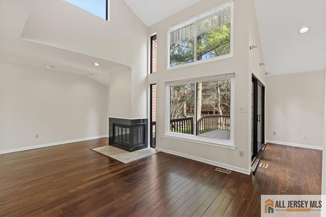 unfurnished living room with a healthy amount of sunlight, high vaulted ceiling, wood-type flooring, and a multi sided fireplace
