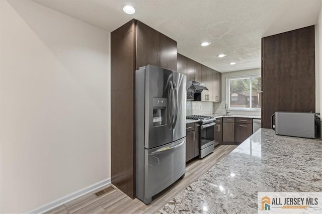 kitchen with appliances with stainless steel finishes, light stone countertops, a sink, light wood-style floors, and under cabinet range hood