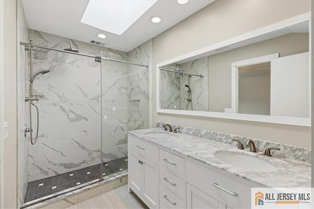 bathroom featuring a skylight, a marble finish shower, recessed lighting, and a sink