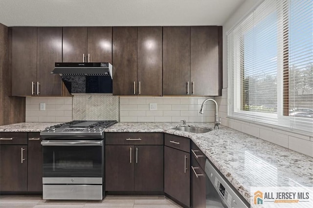 kitchen with dark brown cabinets, tasteful backsplash, light stone counters, a sink, and stainless steel appliances