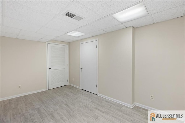 finished basement featuring visible vents, a paneled ceiling, baseboards, and light wood-type flooring
