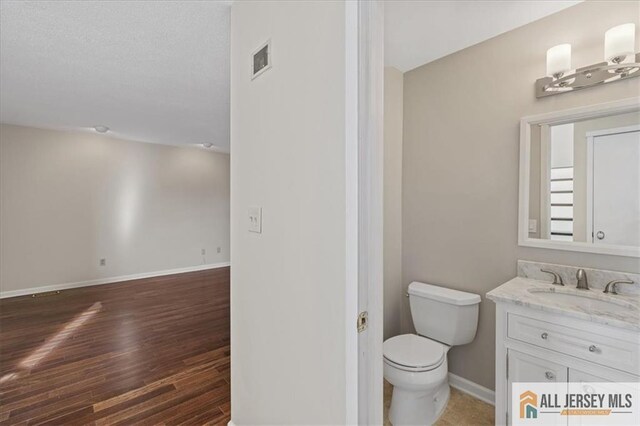 bathroom with visible vents, vanity, wood finished floors, toilet, and baseboards