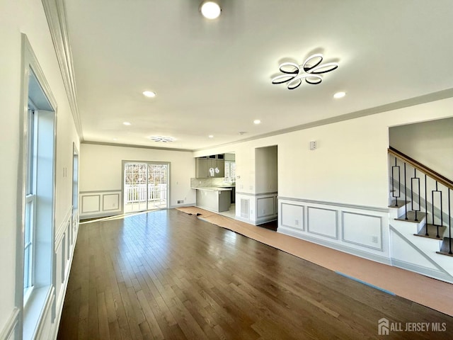 unfurnished living room with stairway, a decorative wall, crown molding, hardwood / wood-style flooring, and recessed lighting