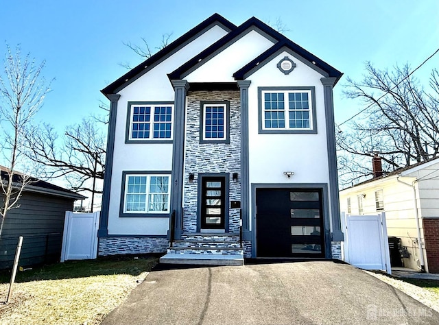 view of front of house with driveway, stone siding, fence, a garage, and stucco siding