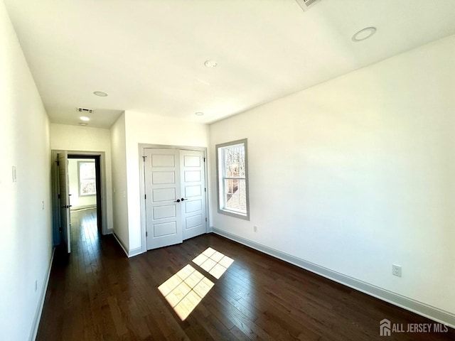 unfurnished bedroom with dark wood-type flooring, a closet, baseboards, and recessed lighting
