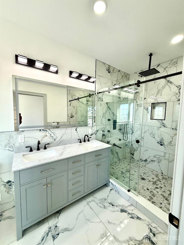 bathroom with double vanity, tile walls, a marble finish shower, and a sink