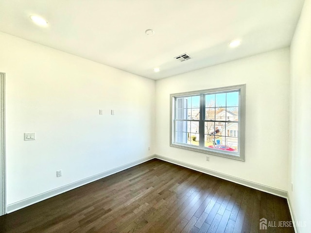 empty room featuring dark wood-type flooring, visible vents, baseboards, and recessed lighting
