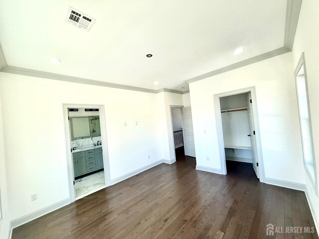 unfurnished bedroom featuring a spacious closet, dark wood-style floors, visible vents, ornamental molding, and baseboards