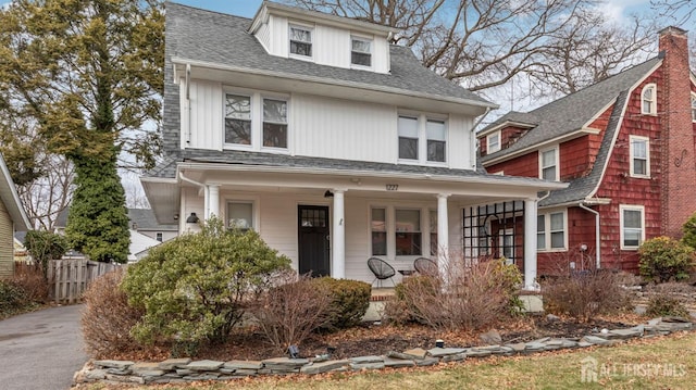 american foursquare style home featuring a porch, roof with shingles, and fence