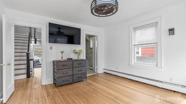 interior space with a baseboard heating unit, multiple windows, and light wood-style flooring