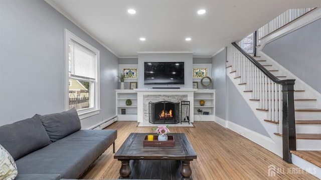 living room featuring a baseboard heating unit, wood finished floors, baseboards, stairs, and crown molding