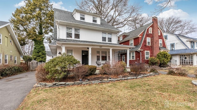 american foursquare style home with aphalt driveway, a front lawn, a porch, and roof with shingles