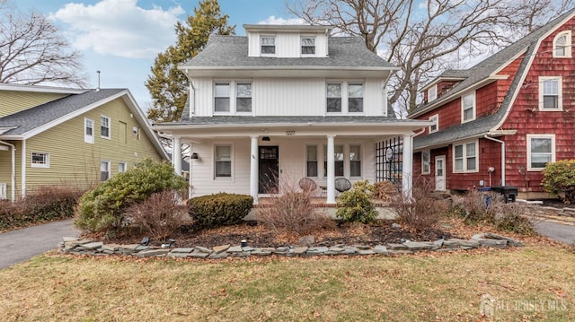 american foursquare style home featuring a porch, roof with shingles, and a front lawn