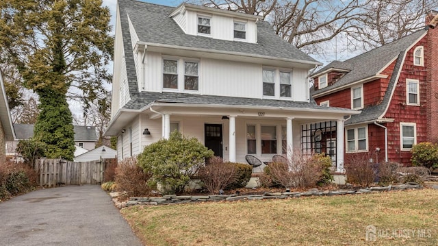 traditional style home with covered porch, a front yard, fence, and roof with shingles