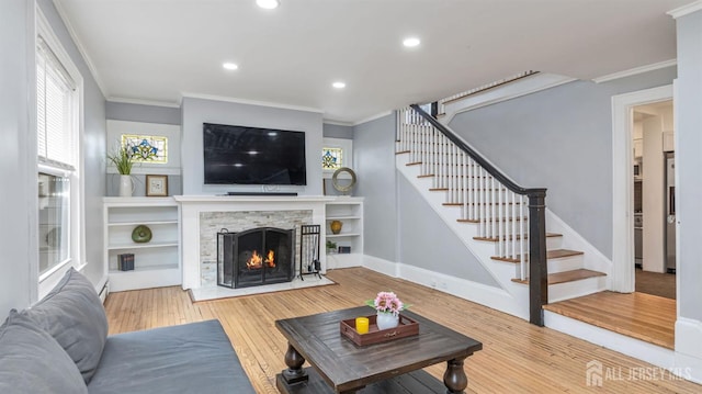 living room with crown molding, stairs, a stone fireplace, recessed lighting, and wood finished floors