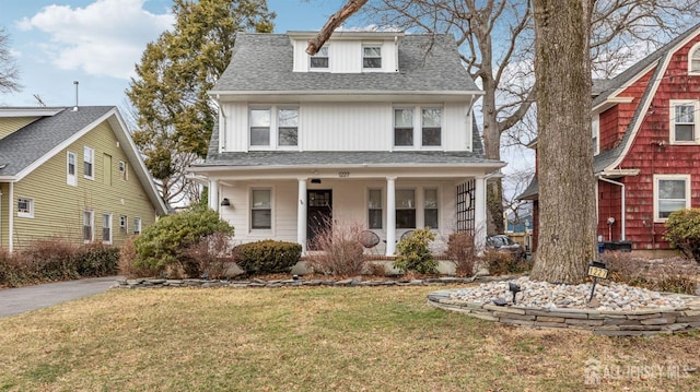 traditional style home with a shingled roof, a front yard, and covered porch