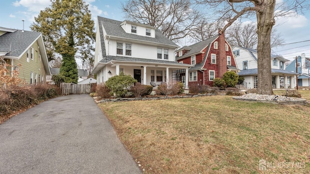 traditional style home featuring a porch, aphalt driveway, fence, roof with shingles, and a front lawn