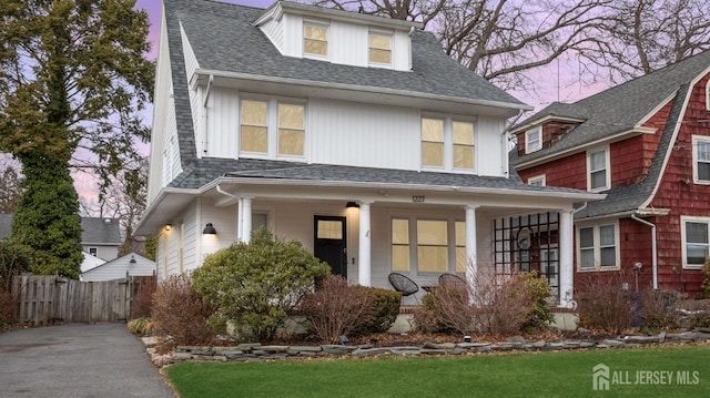 american foursquare style home featuring a shingled roof, fence, and a porch