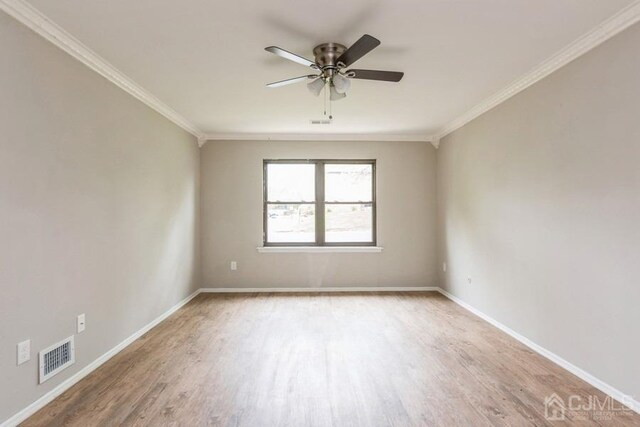 spare room with crown molding, wood finished floors, visible vents, and baseboards