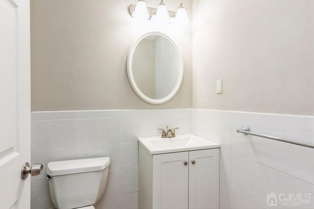 bathroom with toilet, wainscoting, tile walls, and vanity