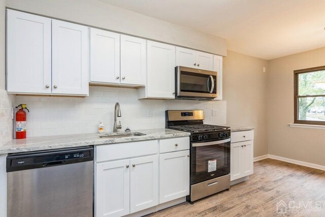 kitchen with light stone counters, appliances with stainless steel finishes, light wood-style floors, white cabinets, and a sink