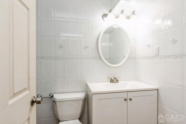 bathroom with toilet, tile walls, and vanity