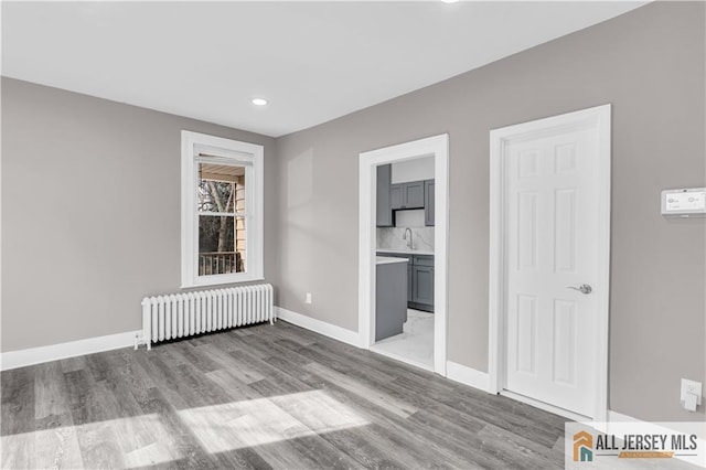 interior space featuring a sink, light wood finished floors, radiator, recessed lighting, and baseboards