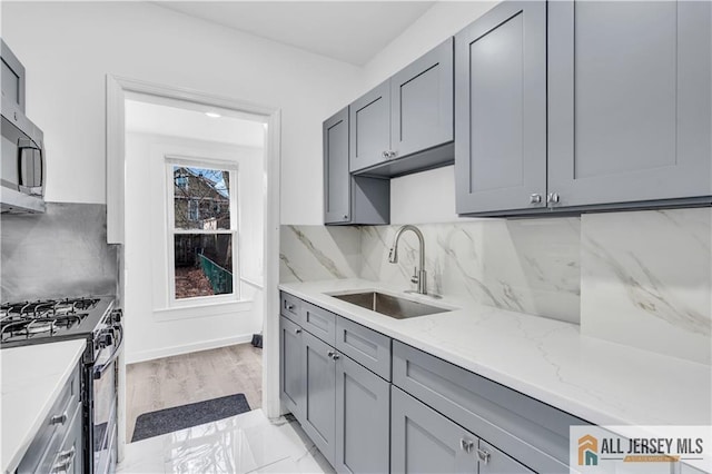 kitchen featuring decorative backsplash, light stone counters, stainless steel appliances, gray cabinetry, and a sink