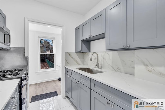 kitchen with backsplash, gas range, light stone countertops, gray cabinetry, and a sink