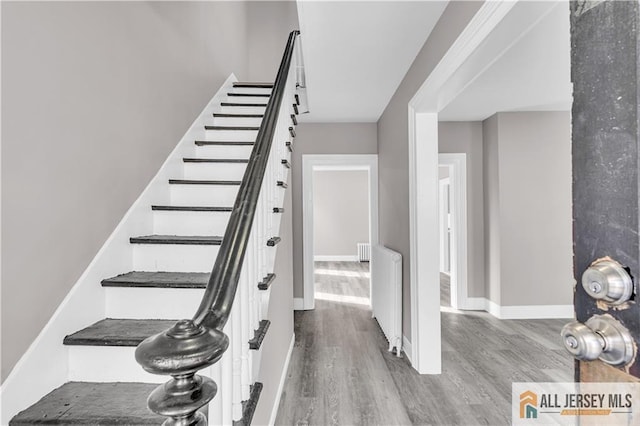 stairs with baseboards, radiator, and wood finished floors
