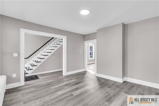 unfurnished living room featuring baseboards, stairs, and wood finished floors