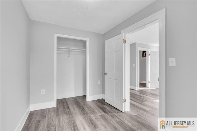 unfurnished bedroom featuring baseboards, wood finished floors, and a closet