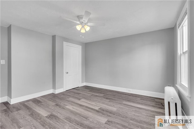 unfurnished room featuring ceiling fan, plenty of natural light, wood finished floors, and radiator