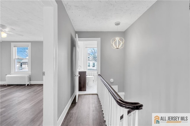 corridor featuring a textured ceiling, wood finished floors, baseboards, an upstairs landing, and radiator heating unit