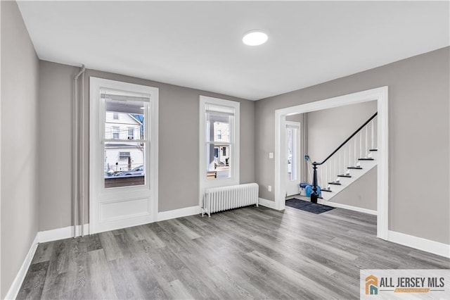 entrance foyer with stairs, radiator heating unit, wood finished floors, and baseboards