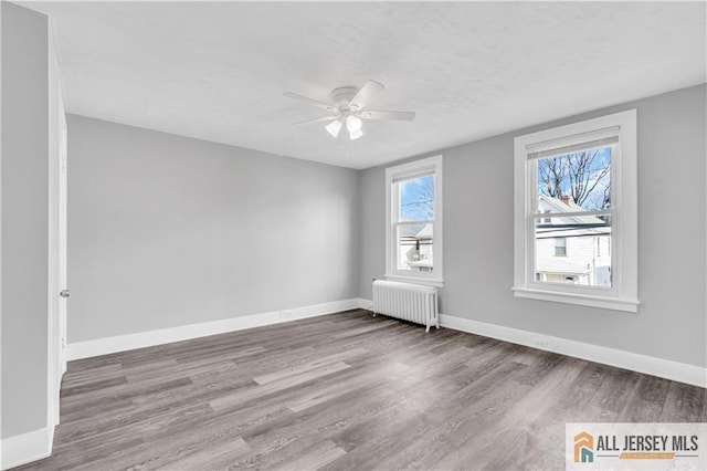 spare room featuring radiator heating unit, wood finished floors, a ceiling fan, and baseboards