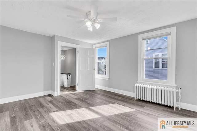 unfurnished bedroom with wood finished floors, baseboards, radiator heating unit, and multiple windows