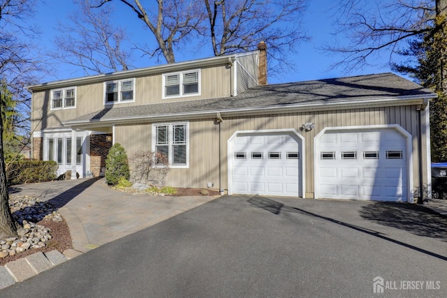 traditional-style house with aphalt driveway, an attached garage, a chimney, and roof with shingles