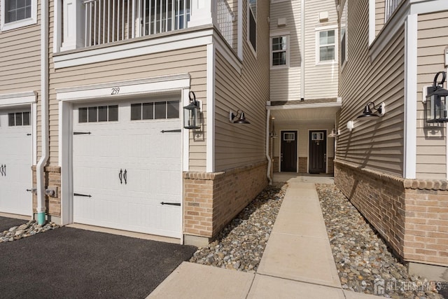 entrance to property featuring a garage, brick siding, and aphalt driveway