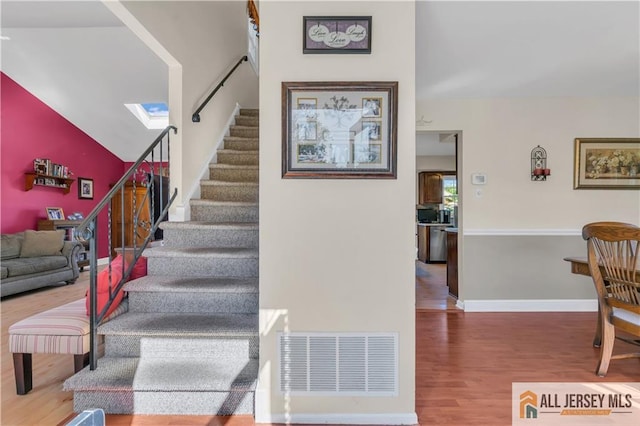 stairway with wood-type flooring and lofted ceiling with skylight