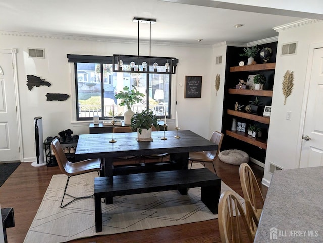 dining room with dark wood-type flooring, visible vents, ornamental molding, and an inviting chandelier