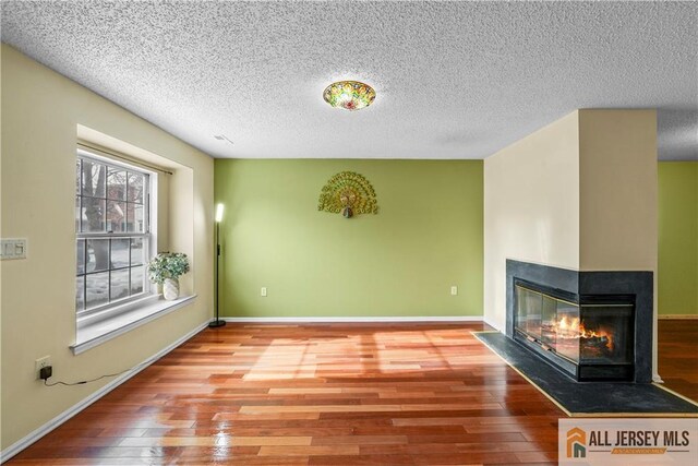 unfurnished living room with hardwood / wood-style flooring, a textured ceiling, and a multi sided fireplace