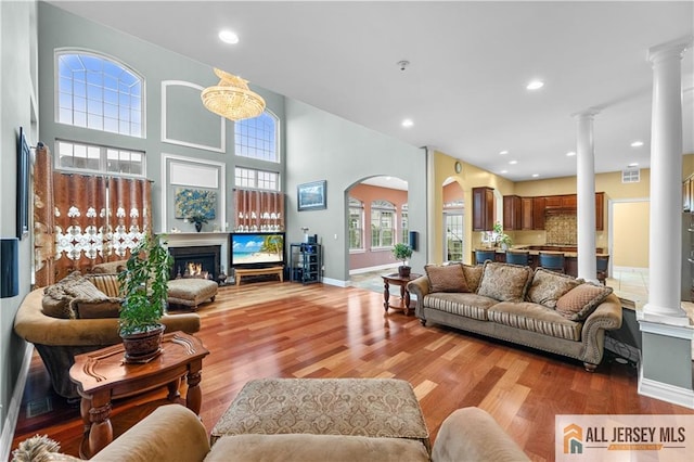 6 Monet Ct, South Brunswick, NJ 08852 - living room with ornate columns, a warm lit fireplace, wood finished floors, arched walkways, and recessed lighting