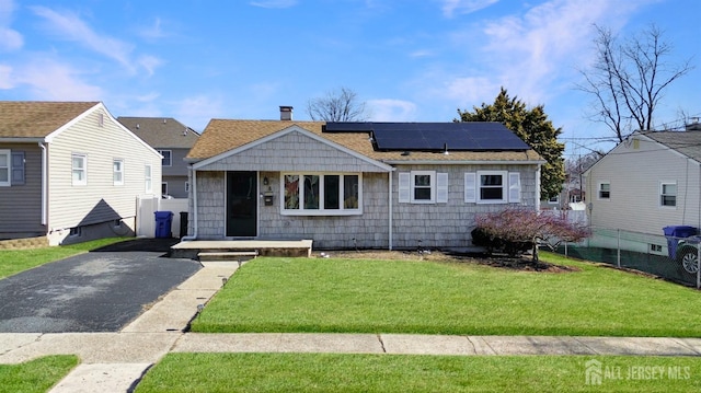 view of front of home with fence, solar panels, a shingled roof, and a front yard